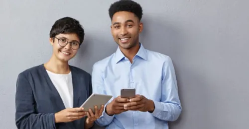 Una mujer joven y un hombre joven sonrientes revisando sus dispositivos electrónicos